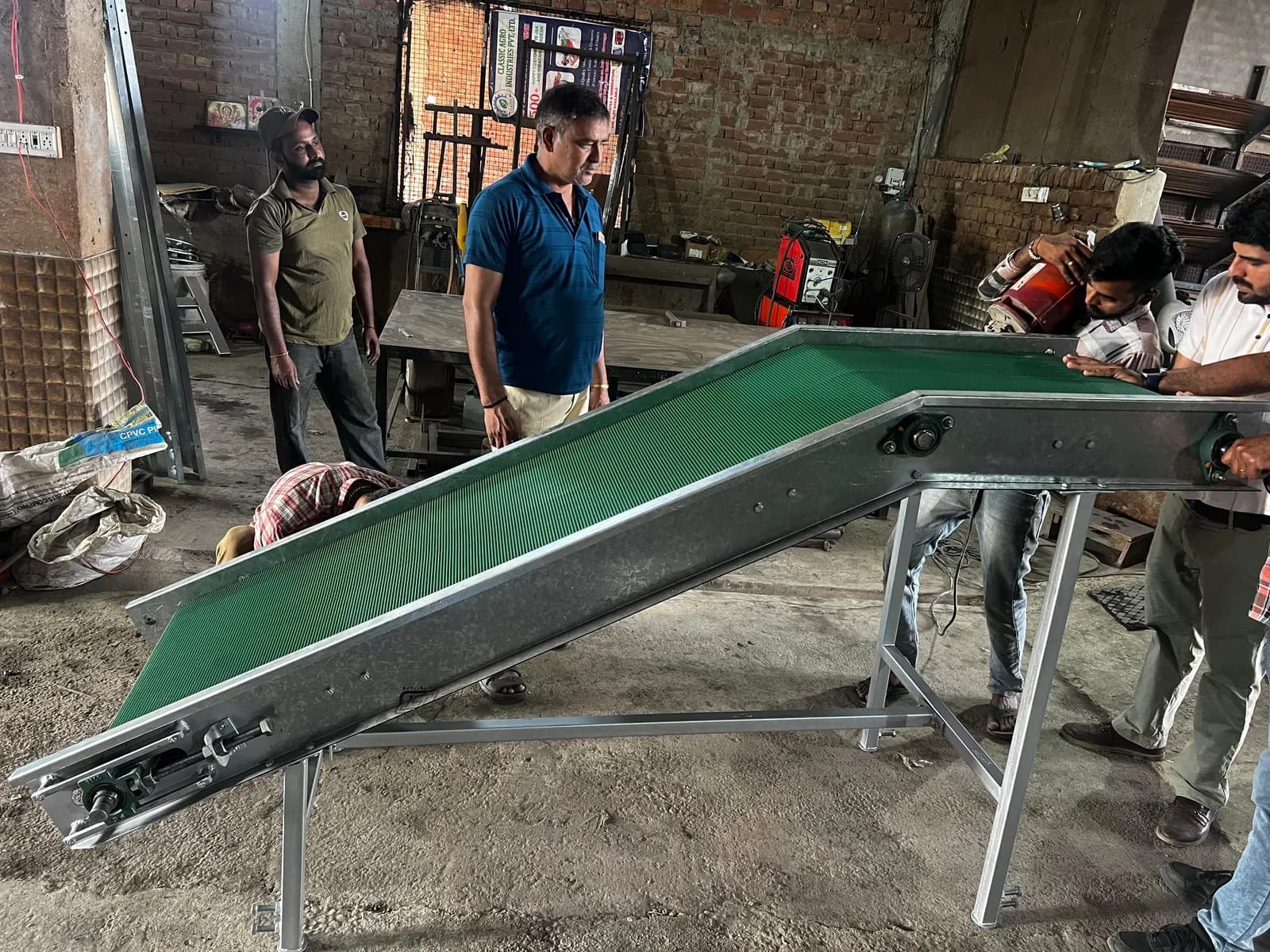 Inclined green belt conveyor on the workshop floor with the team standing around it