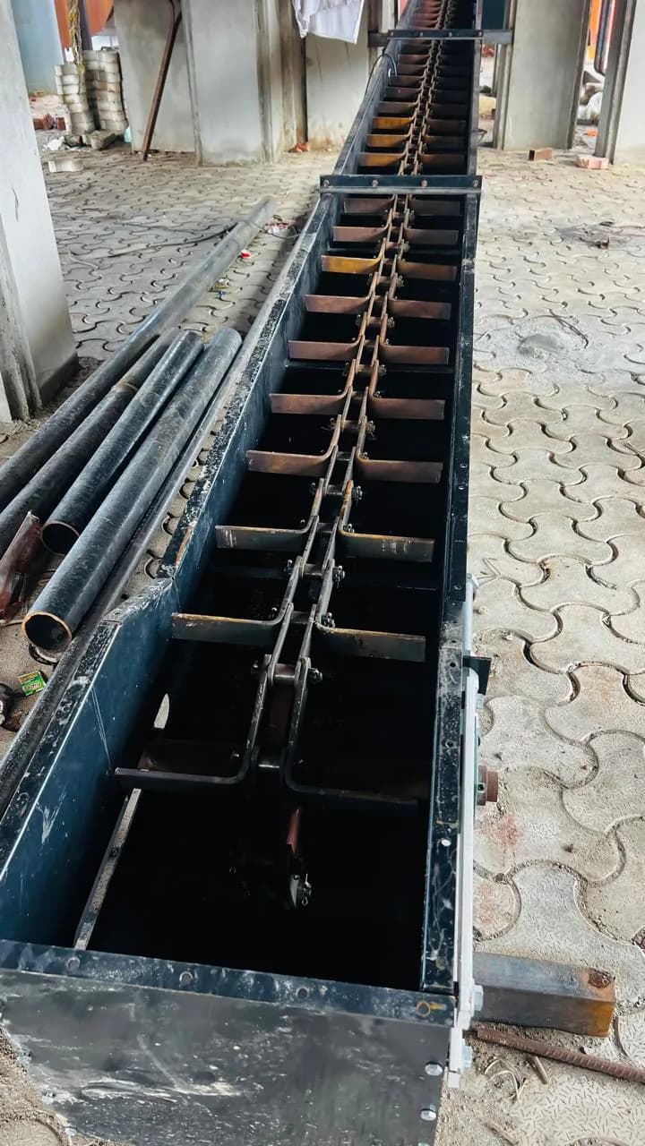 Chain conveyor with paddles running through a channel in a concrete floor