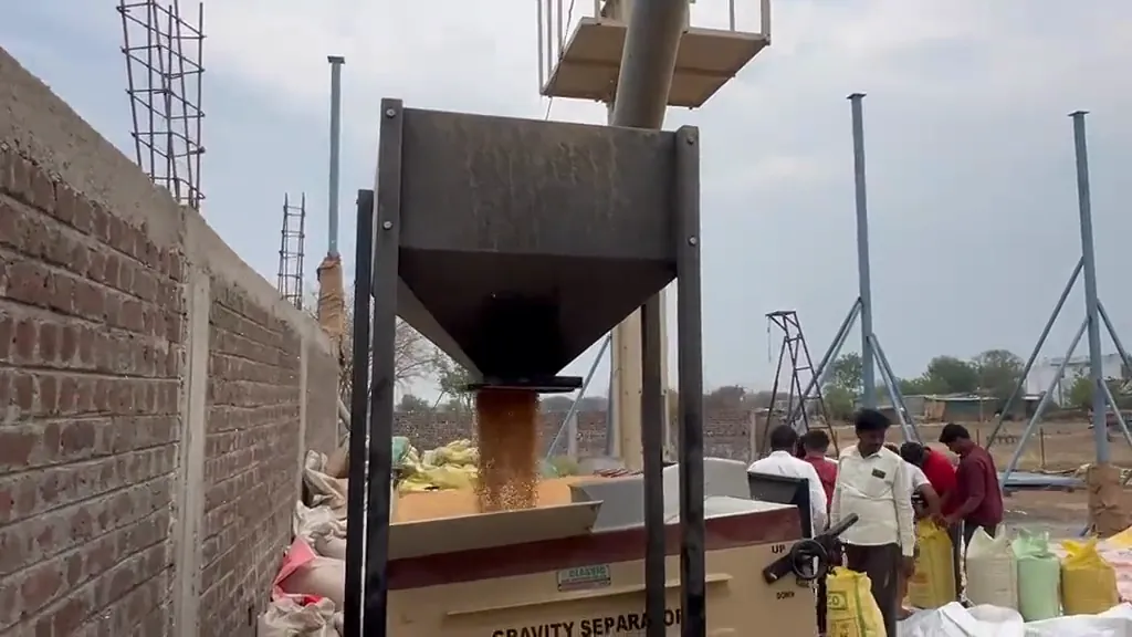 Gravity separator cleaning grain while workers handle bags nearby