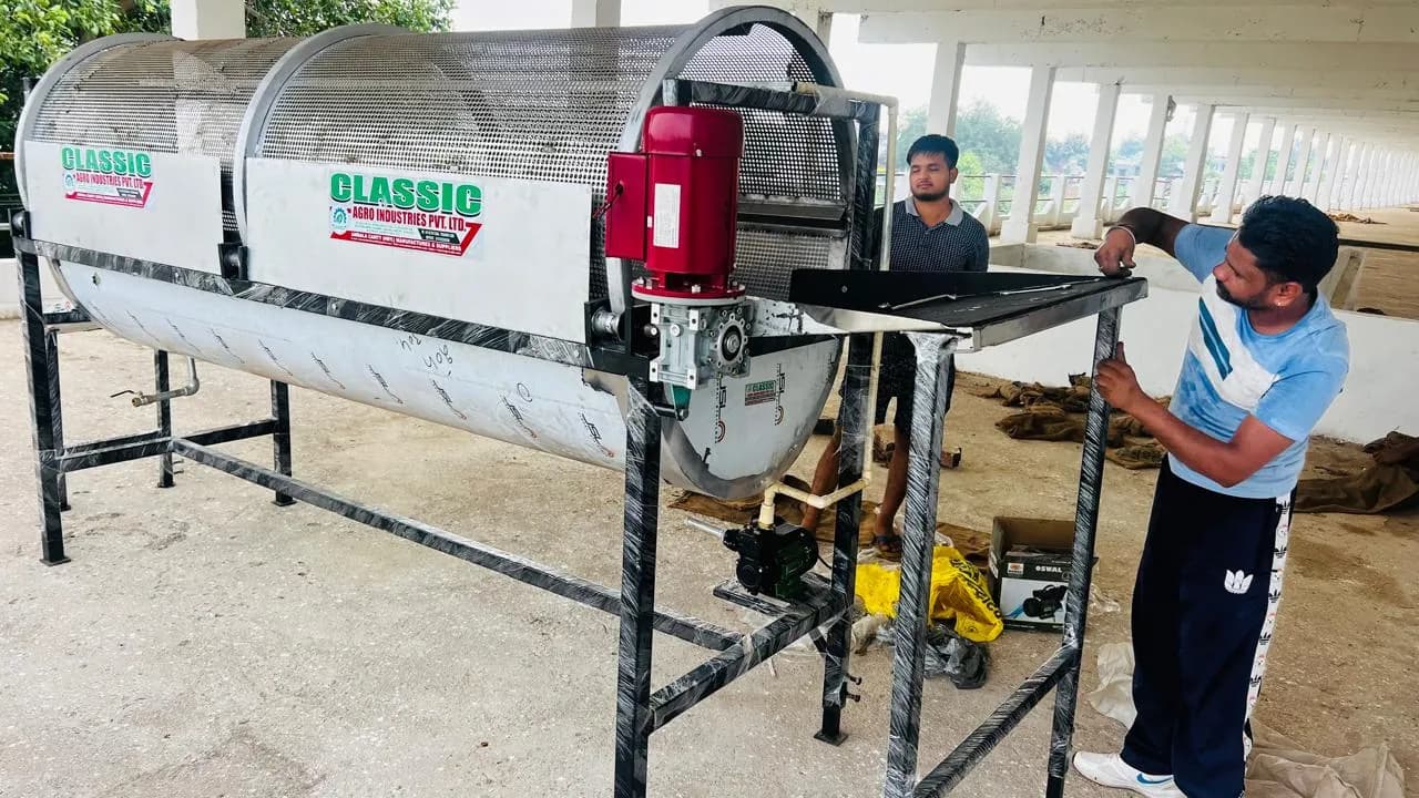 Technician assembling a potato washer machine with a rotating mesh drum and red motor on a steel frame